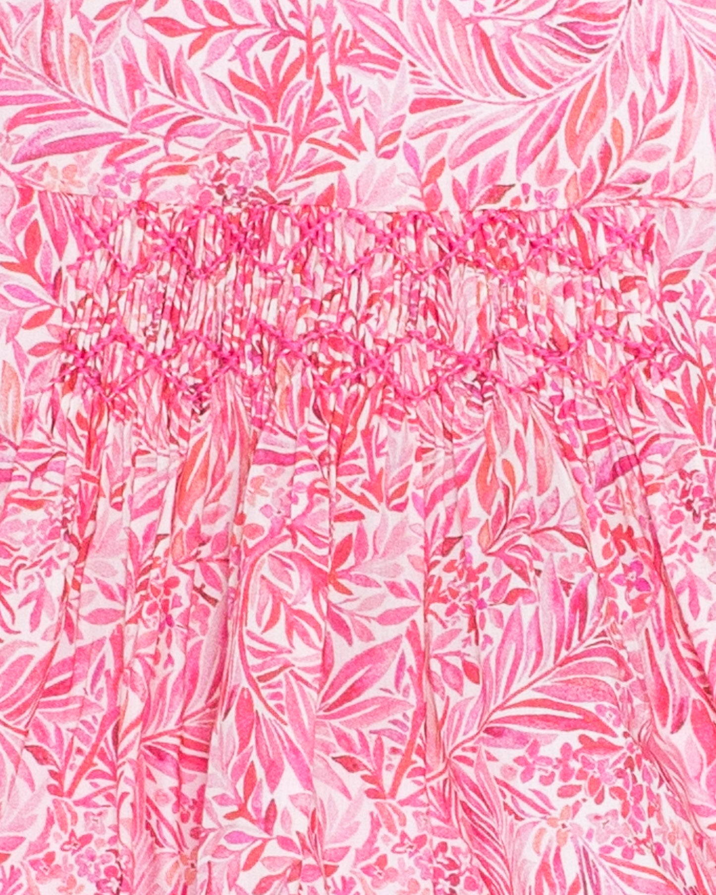 Close-up of the Amelie Liberty Wallace Garden Tunic showing intricate hand-smocking on a vibrant pink Liberty print with leafy floral patterns in light pink and white.