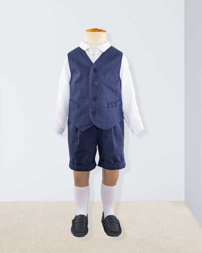 Navy linen suspender shorts and vest styled over a white long-sleeve shirt, shown on a child-sized mannequin with knee-high socks and navy shoes