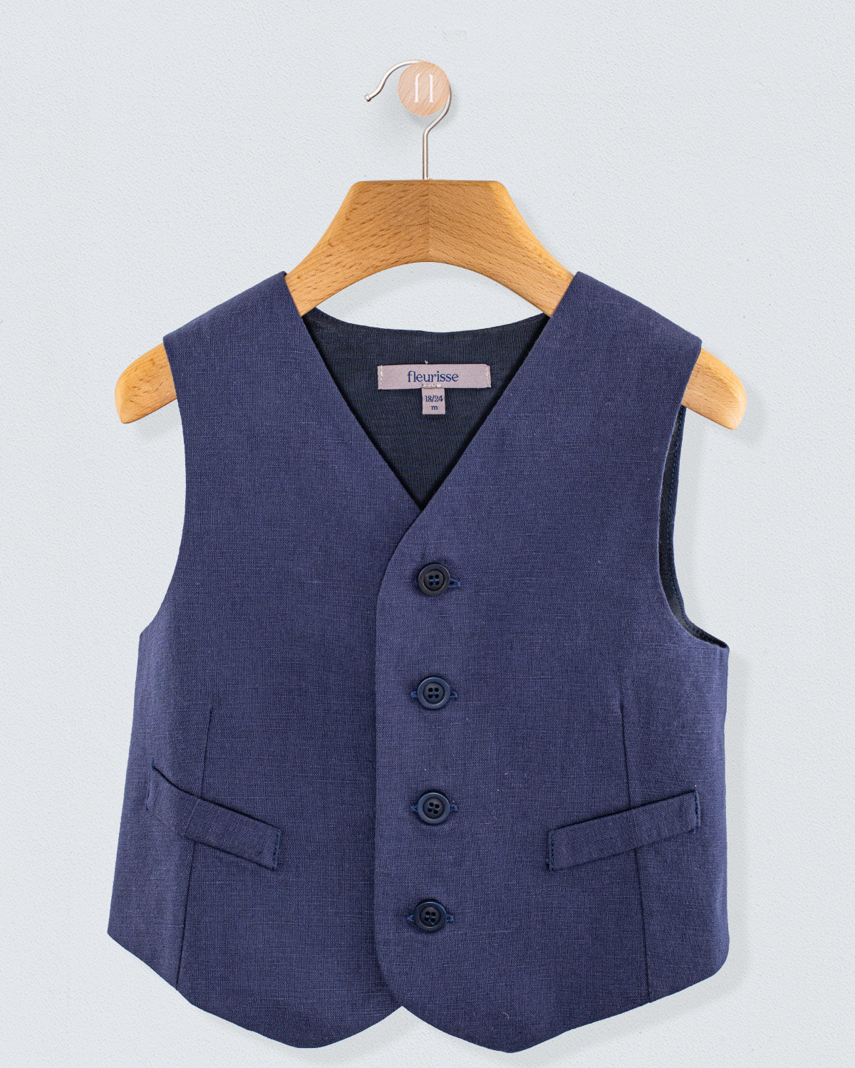 Front view of navy linen vest with three corozo buttons and two front pockets, hanging on a wooden hanger
