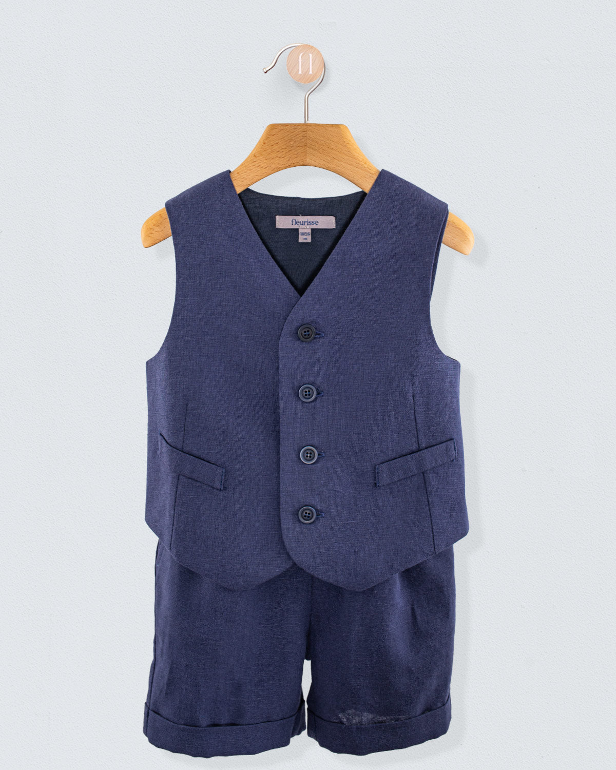 Front view of navy linen suspender shorts with matching vest hanging on a wooden hanger against a light background