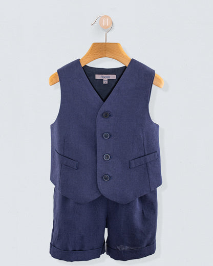 Front view of navy linen suspender shorts with matching vest hanging on a wooden hanger against a light background