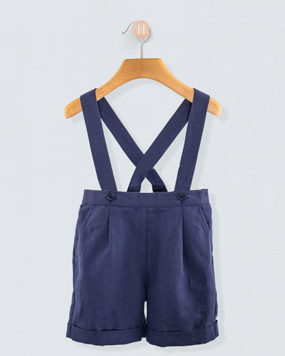 Front view of navy linen suspender shorts with crossed straps and waistband button detail, displayed on a hanger