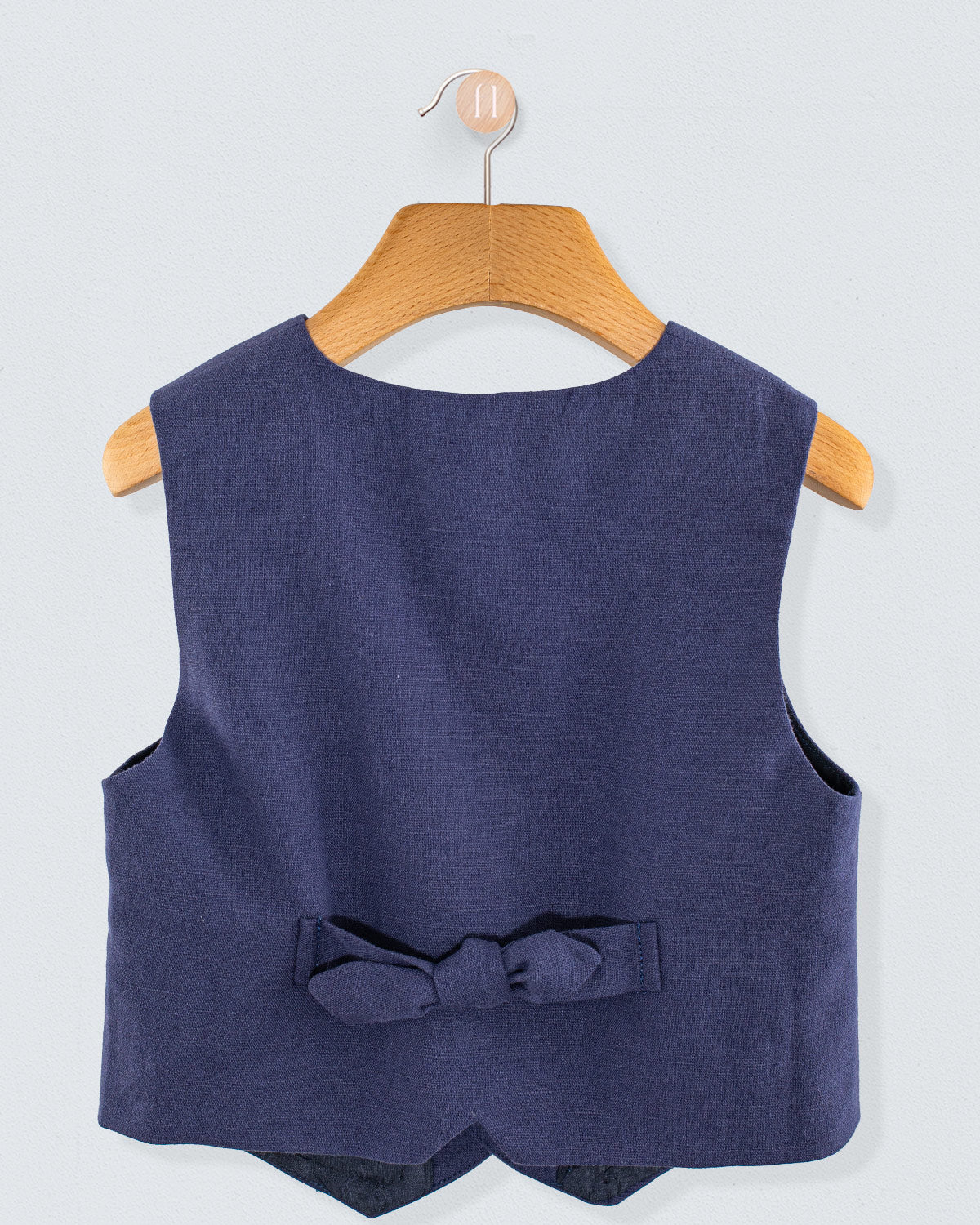 Back view of navy linen vest featuring a decorative bow at the waist, shown on a hanger