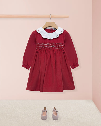 Red dress with white collar on a hanger against a pink background