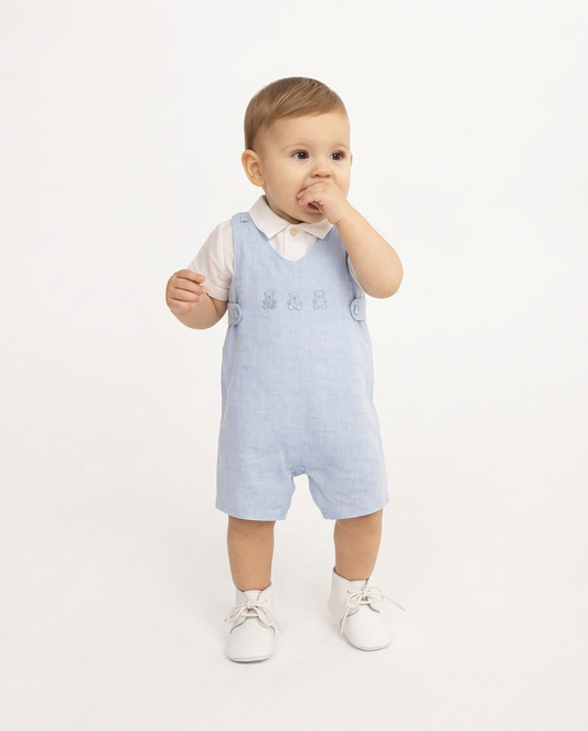 Baby wearing a light blue checkered romper with a white shirt underneath on a white background