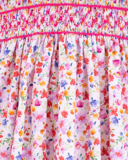 Close-up of the Amandine Veneto Hot Pink Garden Smock showing the hot pink hand-smocking detail and floral pattern with pink, orange, and purple flowers on white cotton.