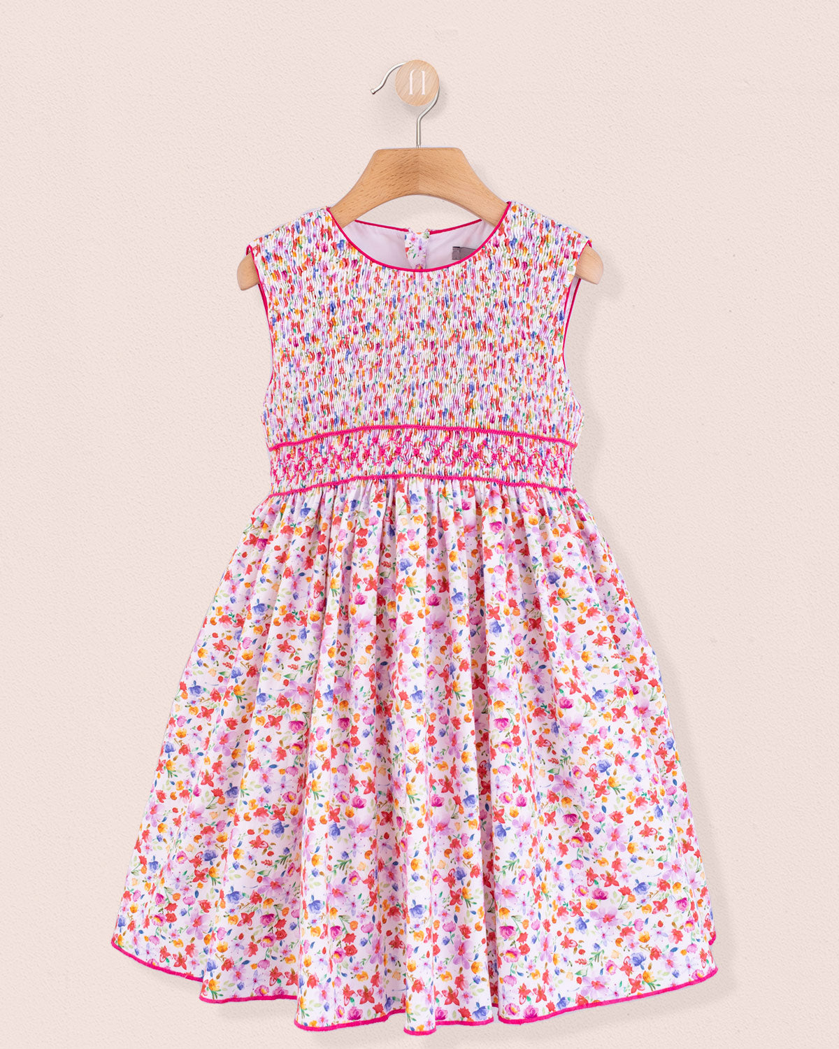 Front view of the Amandine Veneto Hot Pink Garden Smock dress, a sleeveless cotton dress with a hand-smocked bodice and full skirt in a bright multicolor floral print with hot pink trim accents.