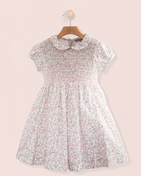 Front view of Amanda Blush Garden Smocked Dress hanging on a wooden hanger against a pink wall