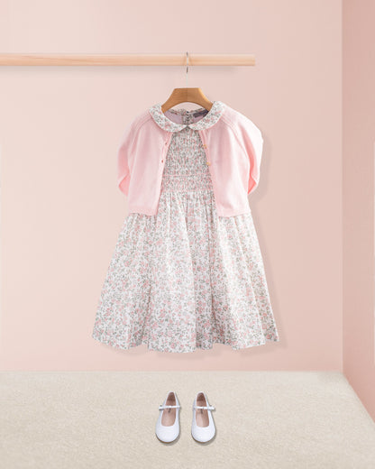 Amanda Blush Garden Smocked Dress styled with a pink cardigan and white shoes on a pink wall background
