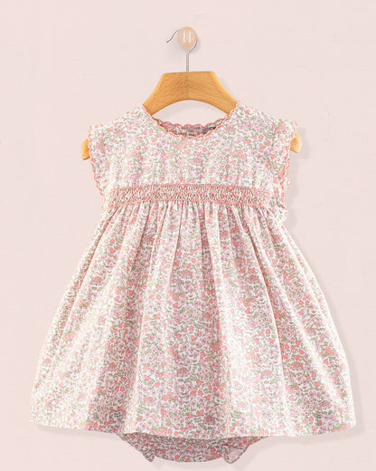 Baby Amelie Garden Pink Set front view featuring a pink floral smocked dress with cap sleeves and gathered skirt on a wooden hanger against a pale pink wall