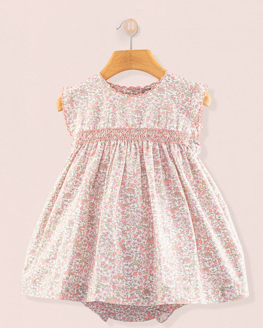 Baby Amelie Garden Pink Set front view featuring a pink floral smocked dress with cap sleeves and gathered skirt on a wooden hanger against a pale pink wall