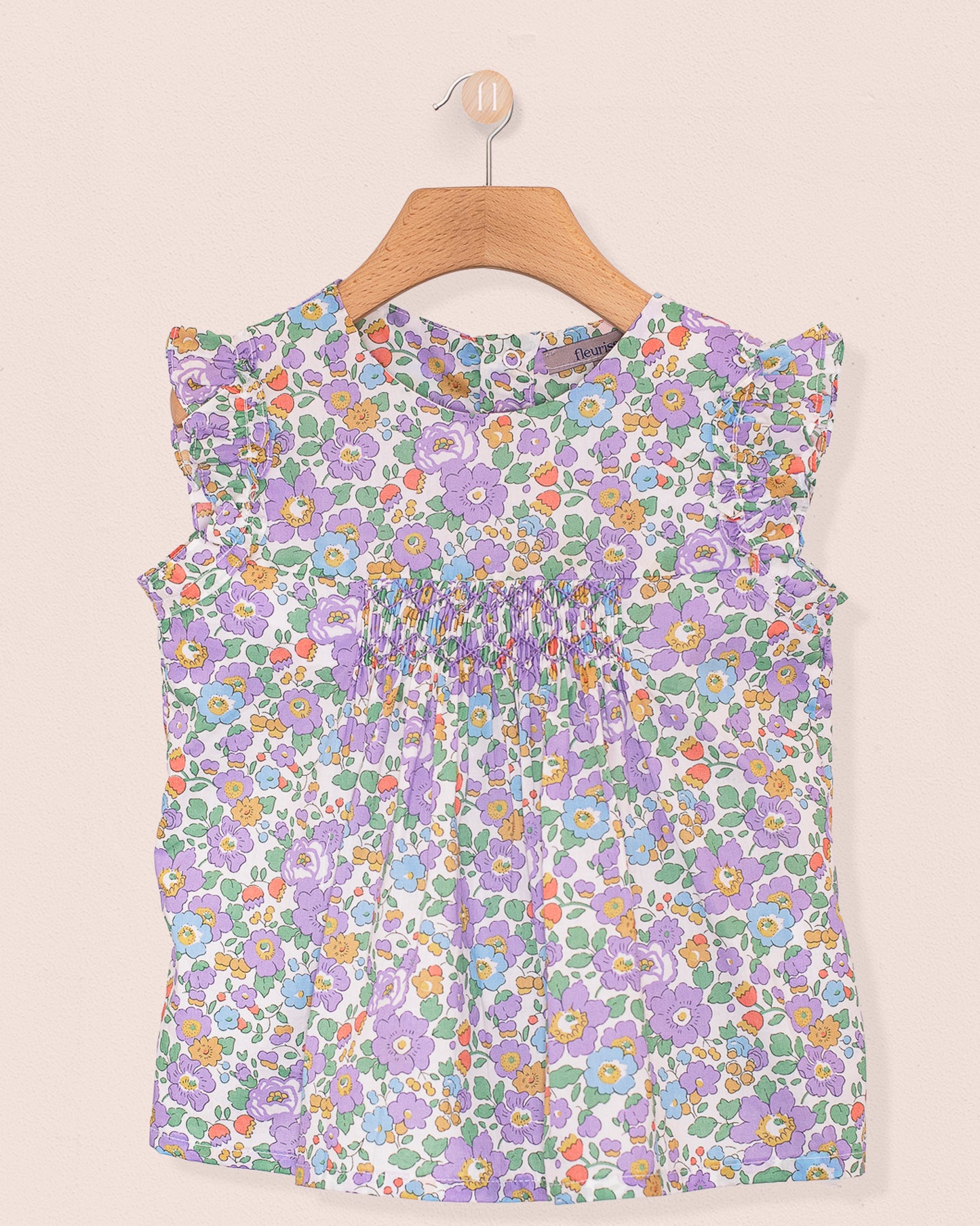 Front view of the Amelie Liberty Betsy Lavender Tunic, a sleeveless A-line top with hand-smocked detailing at the chest and ruffled sleeves in a lavender, green, and orange floral Liberty of London print.
