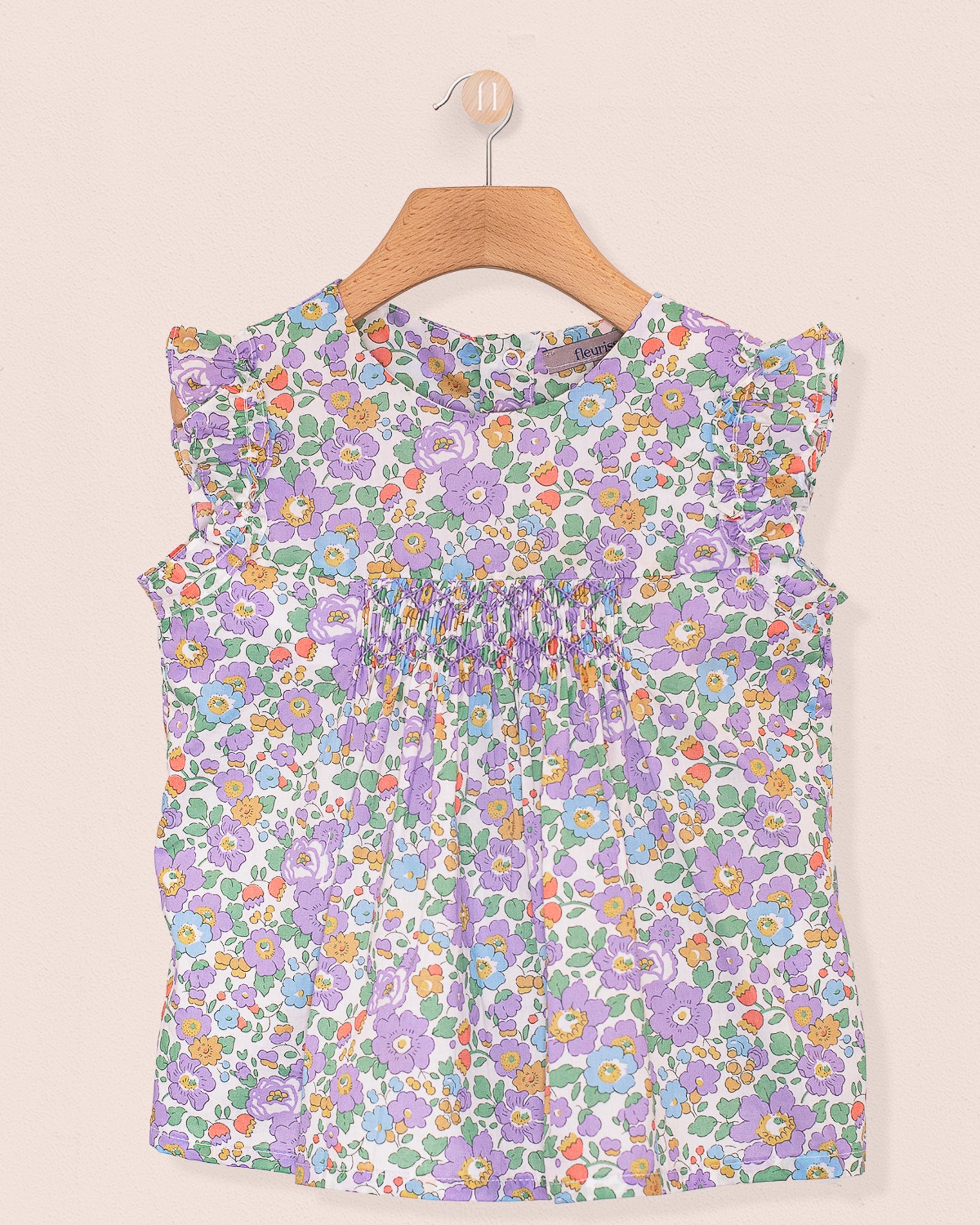 Front view of the Amelie Liberty Betsy Lavender Tunic, a sleeveless A-line top with hand-smocked detailing at the chest and ruffled sleeves in a lavender, green, and orange floral Liberty of London print.