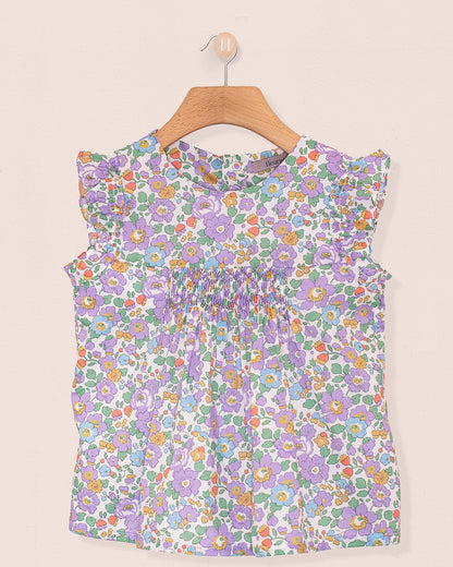 Front view of the Amelie Liberty Betsy Lavender Tunic, a sleeveless A-line top with hand-smocked detailing at the chest and ruffled sleeves in a lavender, green, and orange floral Liberty of London print.