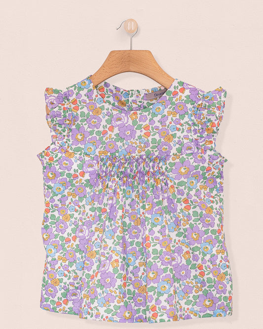 Front view of the Amelie Liberty Betsy Lavender Tunic, a sleeveless A-line top with hand-smocked detailing at the chest and ruffled sleeves in a lavender, green, and orange floral Liberty of London print.
