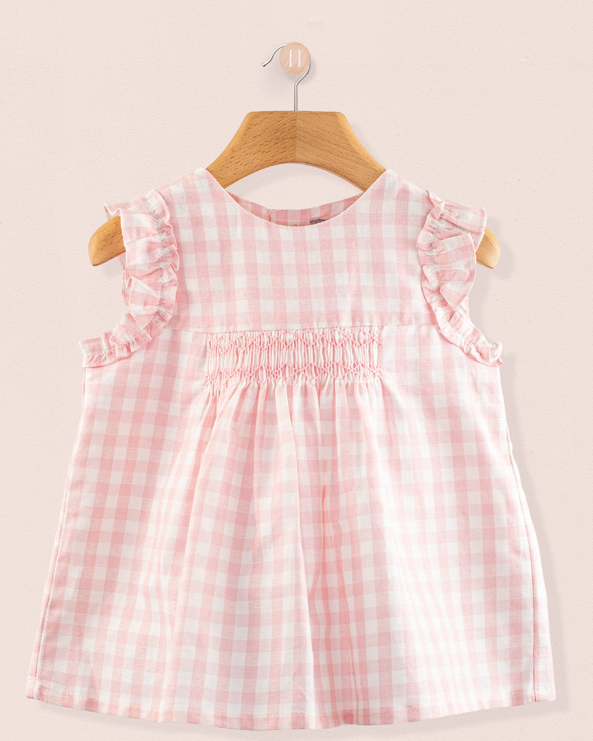 Front view of the Amelie Pink Gingham Linen Tunic, a sleeveless A-line top with hand-smocked detailing, soft ruffled sleeves, and a pale pink and white gingham check pattern.