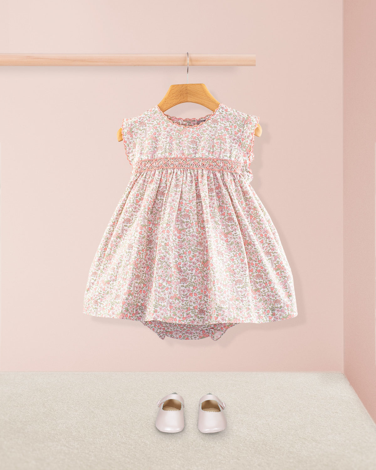 Baby Amelie Garden Pink Set styled with matching bloomers and pink Mary Jane shoes displayed against a pink wall and beige carpet