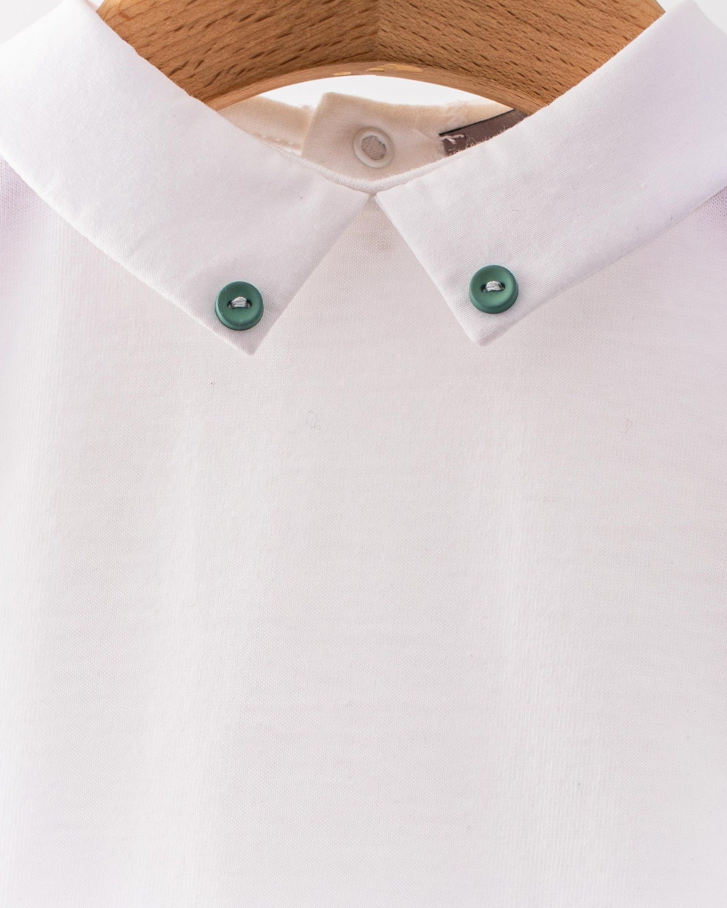 Close-up of the Andreas Onesie collar showing two small hunter green corzo buttons stitched into the tips of the white collar.