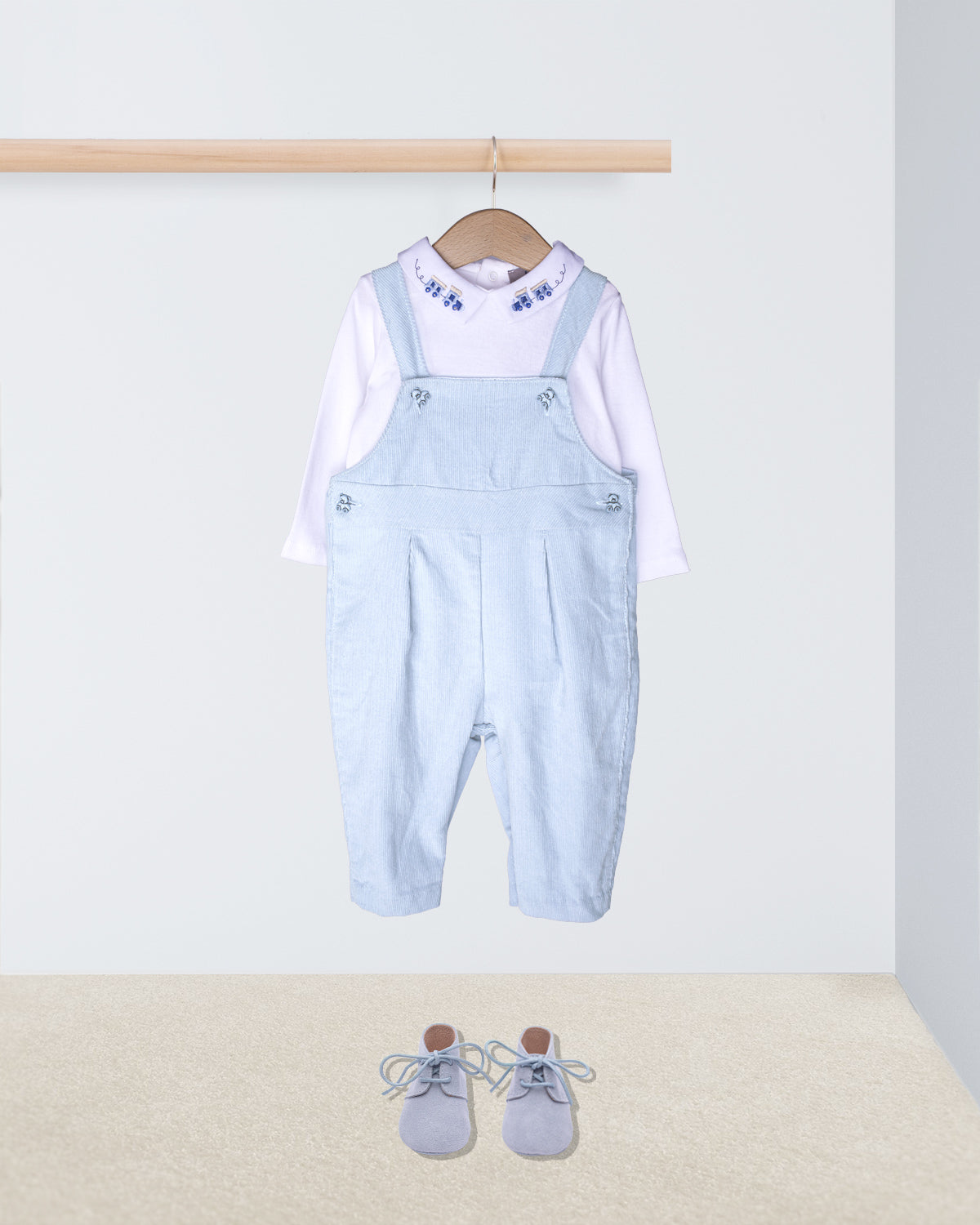 Light blue denim overalls with a white shirt on a hanger, accompanied by gray shoes on the floor.