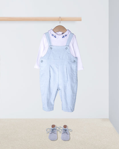 Light blue denim overalls with a white shirt on a hanger, accompanied by gray shoes on the floor.