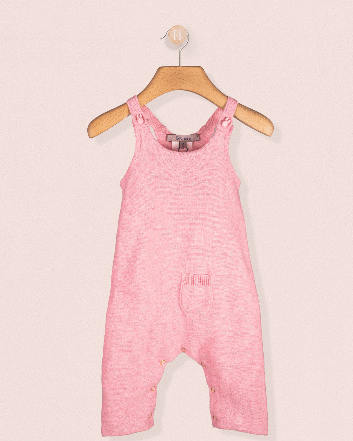Aspen Candy Mélange pink cotton knit overall hanging on a wooden hanger with front pocket detail