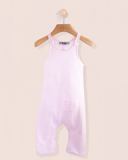 Light pink cotton knit baby overall hanging on a wooden hanger against a pale pink background