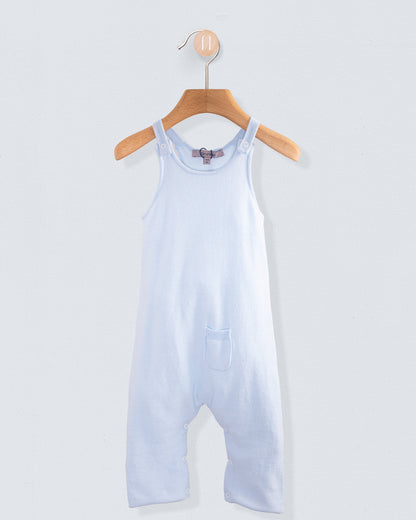 Aspen Powder Blue Cotton Knit Overall hanging on a wooden hanger against a light gray wall. The sleeveless, lightweight cotton one-piece features shoulder straps, a chest pocket, and a soft powder blue color.