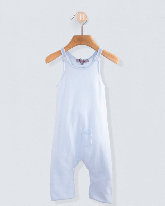 Aspen Powder Blue Cotton Knit Overall hanging on a wooden hanger against a light gray wall. The sleeveless, lightweight cotton one-piece features shoulder straps, a chest pocket, and a soft powder blue color.