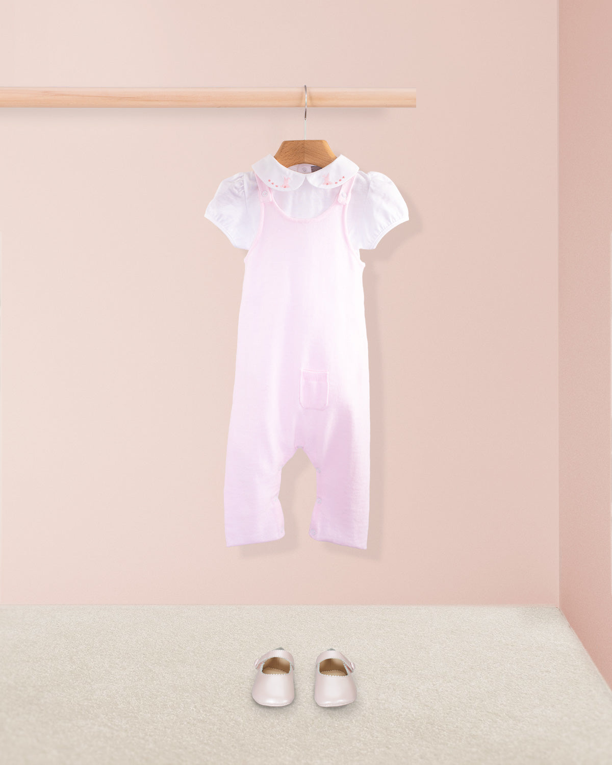 Pink cotton knit baby overall styled with a white embroidered collar onesie and pink baby shoes placed on a beige carpet