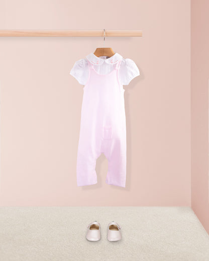 Pink cotton knit baby overall styled with a white embroidered collar onesie and pink baby shoes placed on a beige carpet