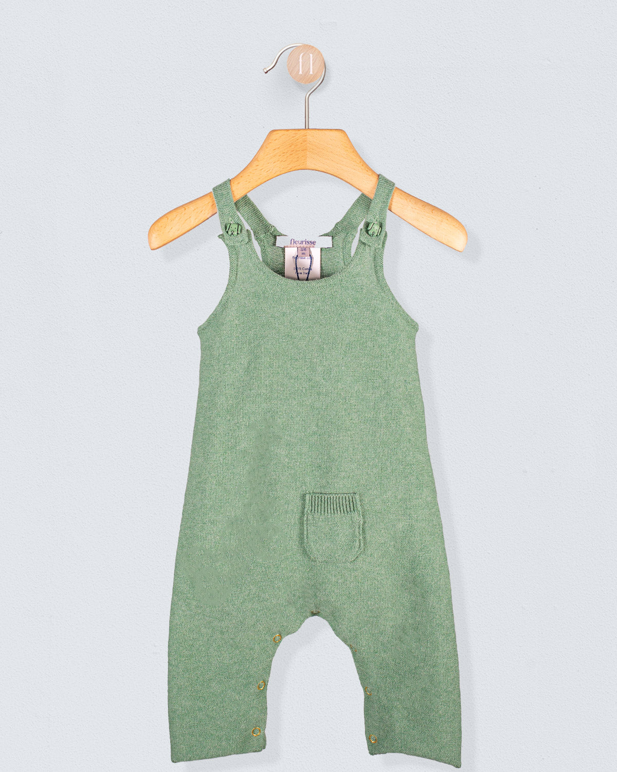 Aspen Sage Melange Cotton Knit Overall hanging on a wooden hanger against a light blue background
