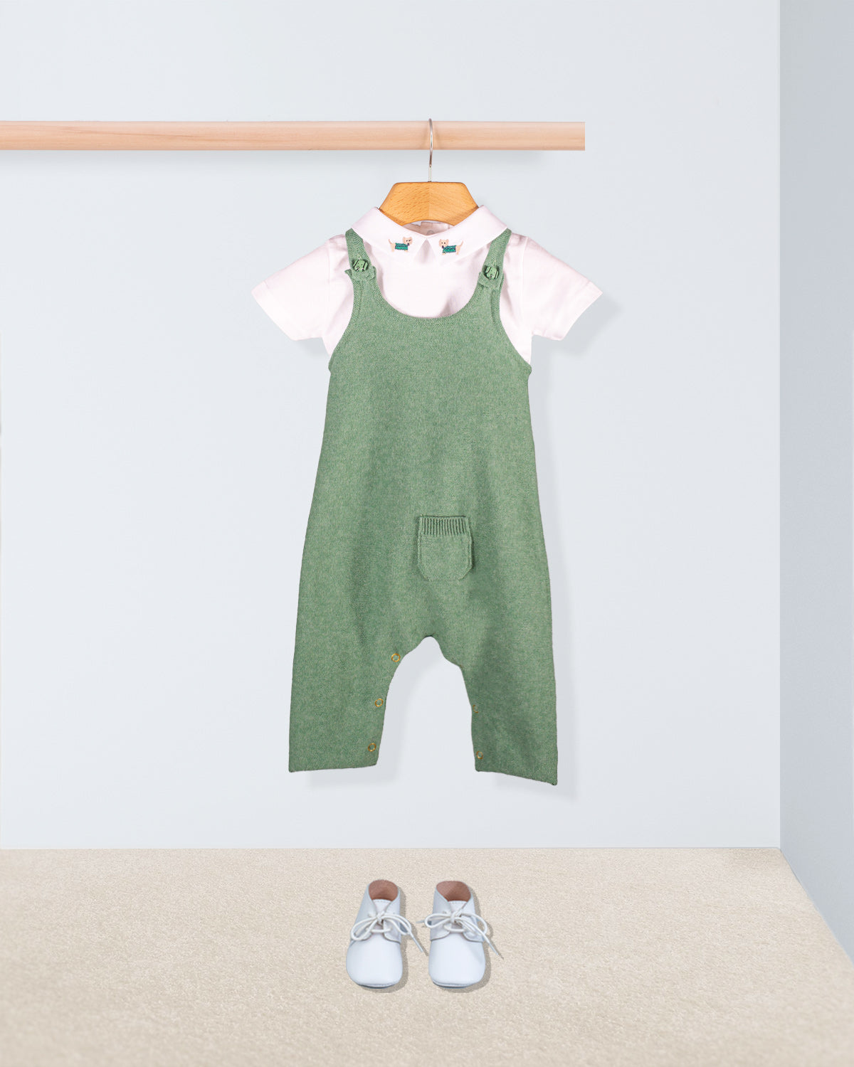 Aspen Sage Melange Cotton Knit Overall styled with a white embroidered collar onesie and white shoes laid out on a beige carpet