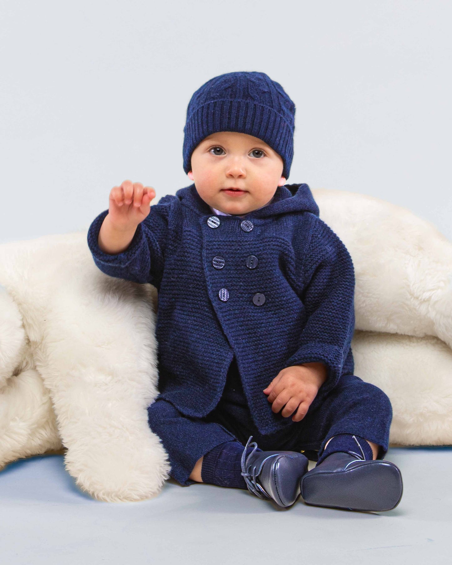 Baby sitting, turned to the front, wearing Chamonix Navy Cashmere Hooded Jacket with matching cashmere hat and pants, showing the front of the jacket