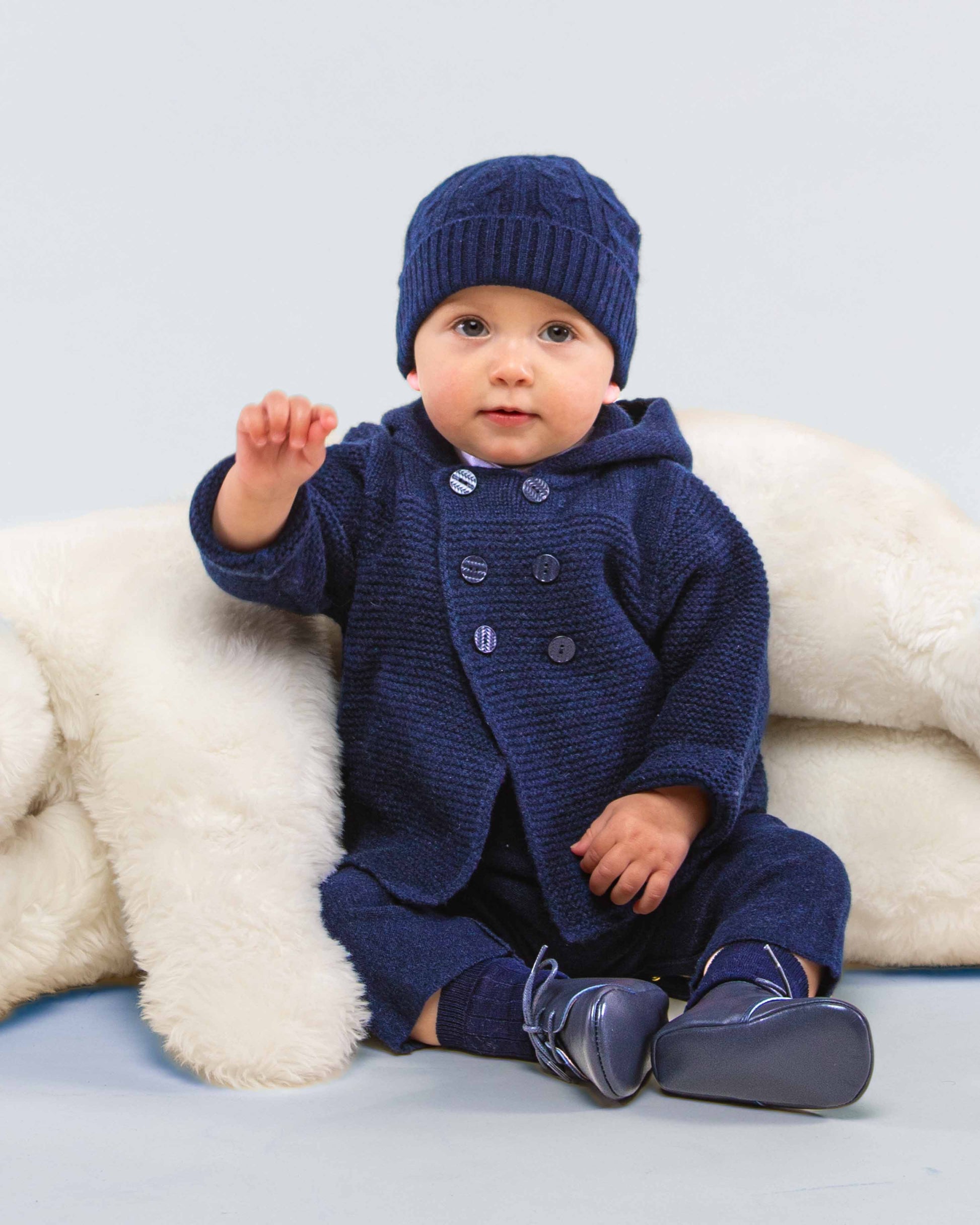 Baby sitting, turned to the front, wearing Chamonix Navy Cashmere Hooded Jacket with matching cashmere hat and pants, showing the front of the jacket