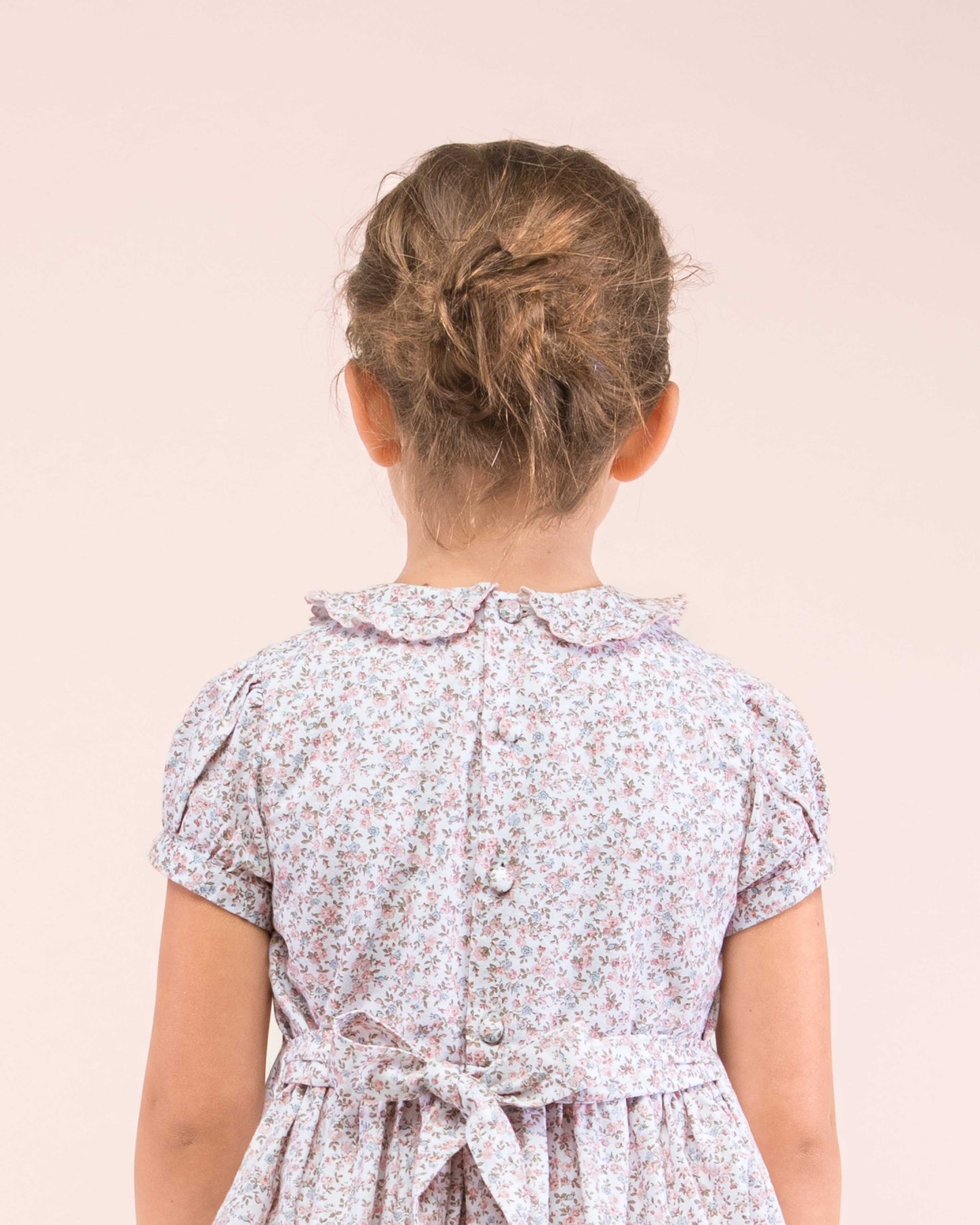 Girl standing wearing the Valentine French Antique Pink Smock dress facing away showing the details of the back of the dress