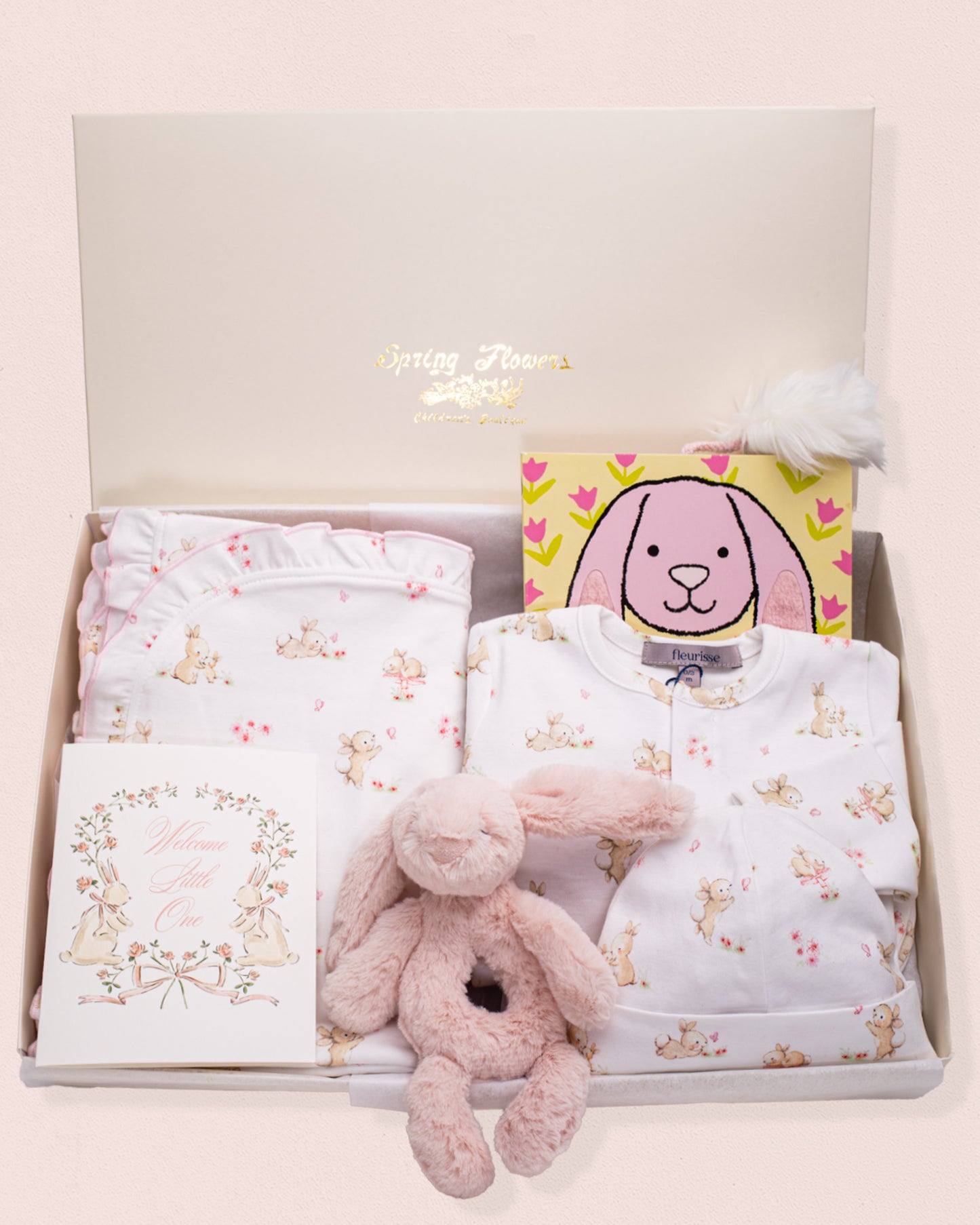Baby Bunnies Gift Bundle featuring a white Pima cotton bunny print footie with matching hat and blanket, a pink Jellycat bunny plush rattle toy, a pink bunny book, and a floral "Welcome Little One" greeting card, all arranged in an open gift box