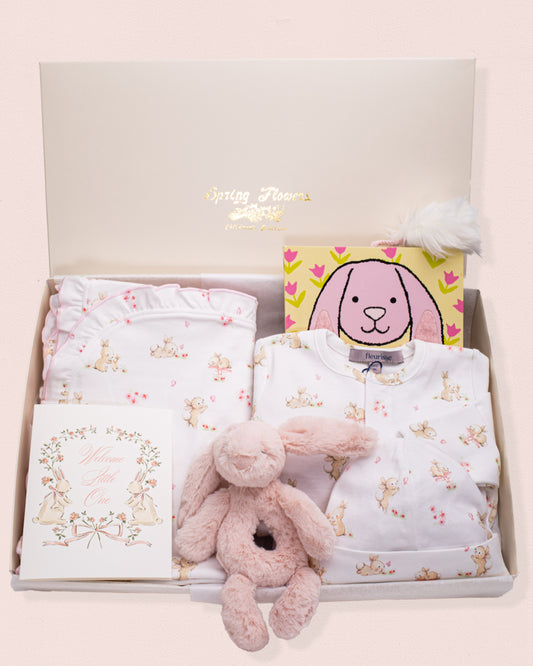 Baby Bunnies Gift Bundle featuring a white Pima cotton bunny print footie with matching hat and blanket, a pink Jellycat bunny plush rattle toy, a pink bunny book, and a floral "Welcome Little One" greeting card, all arranged in an open gift box