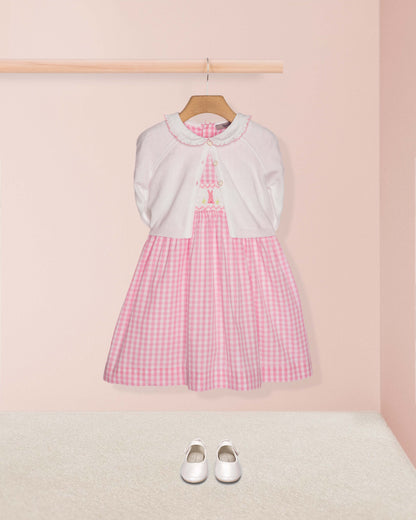 Pink checkered dress with white sweater on a hanger against a pink wall.