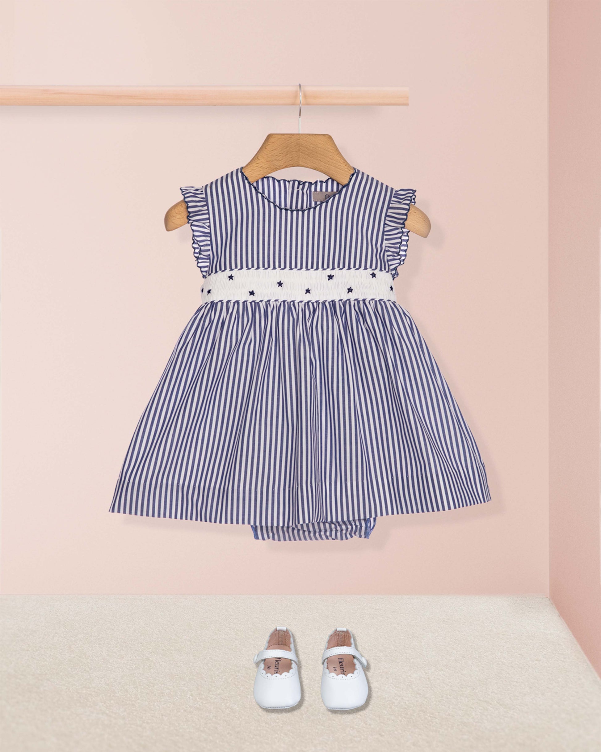 Blue and white striped dress with a belt on a wooden hanger against a pink wall.
