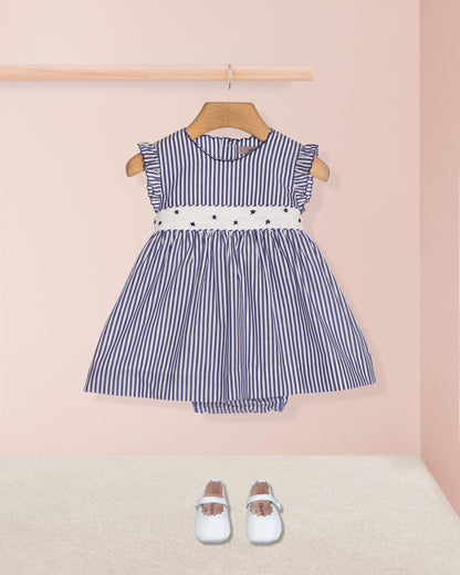 Blue and white striped dress with a belt on a wooden hanger against a pink wall.