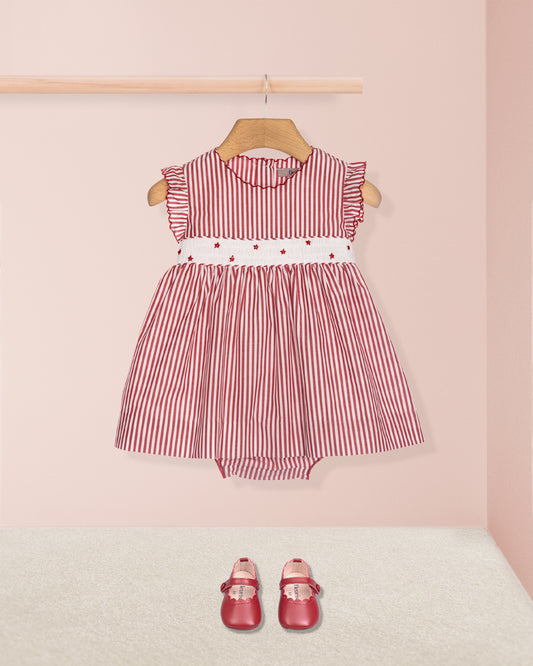 Red and white striped dress with a white belt on a hanger against a pink wall.