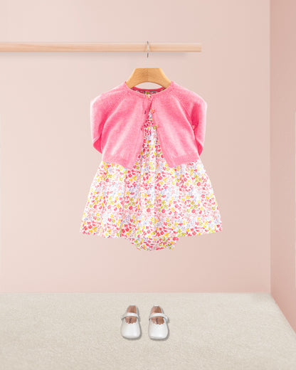 Baby Amelie floral dress styled with primrose pink cardigan and white Mary Jane shoes under a wooden rail