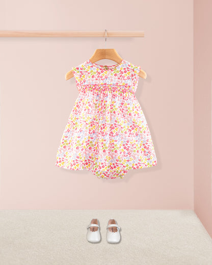 Baby Amelie floral dress shown with matching bloomers and white Mary Jane shoes displayed under a wooden rail