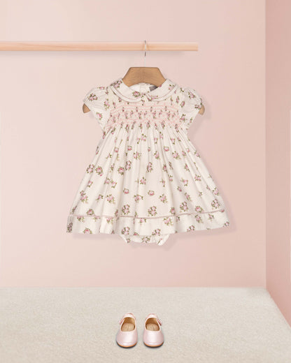 Floral dress on a hanger with pink shoes on the floor against a pink wall