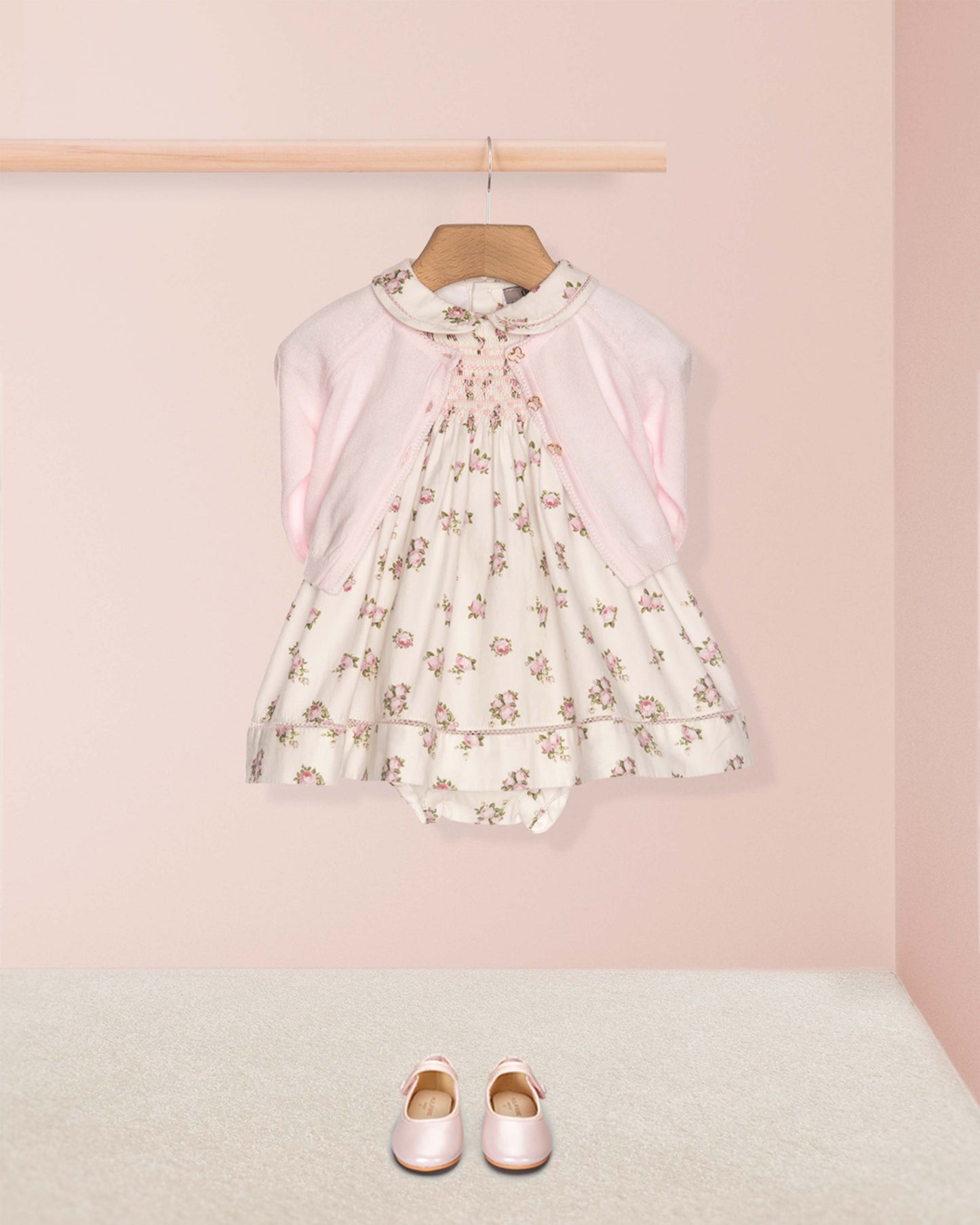 Floral dress on a hanger with pink shoes on the floor against a pink wall