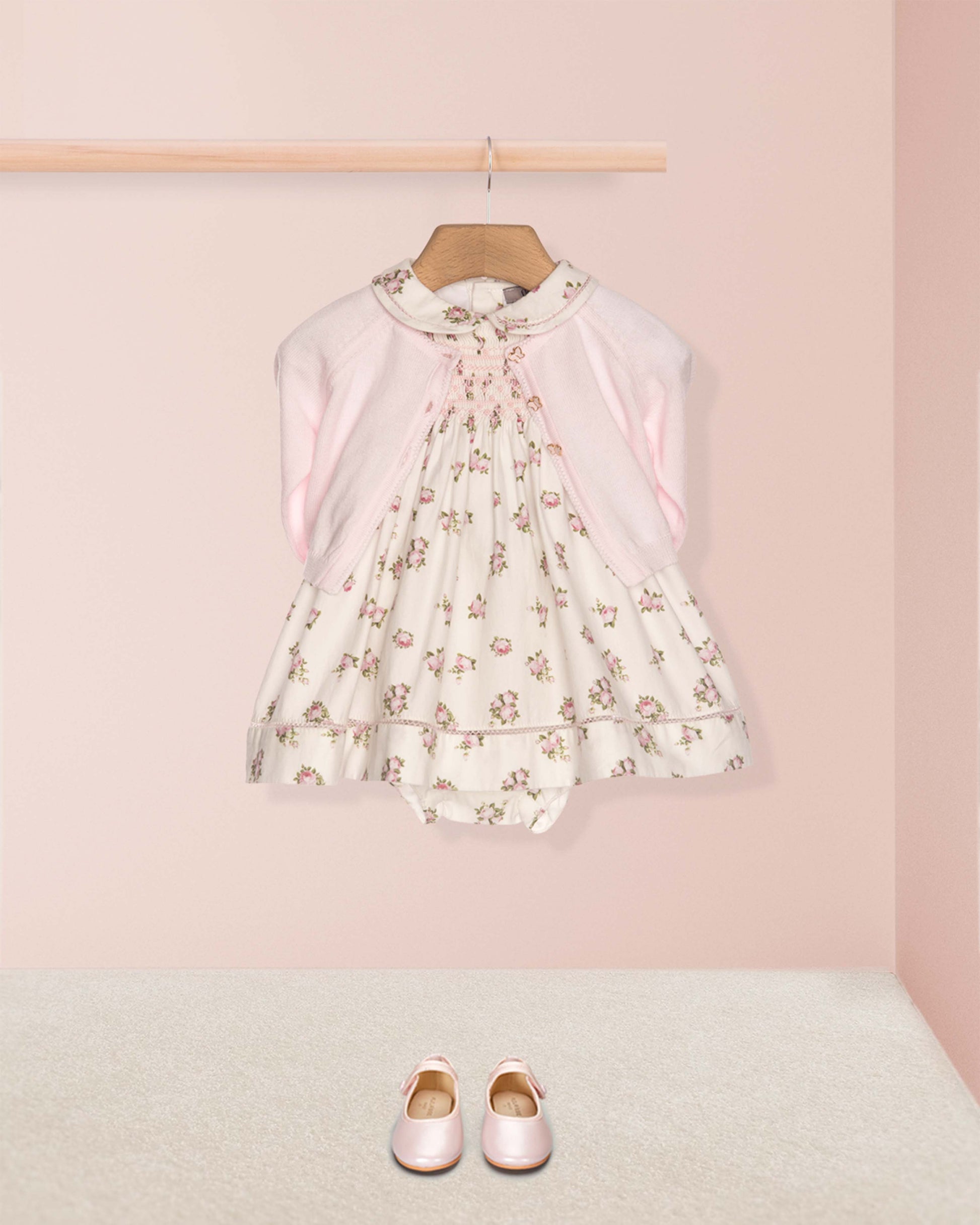 Floral dress on a hanger with pink shoes on the floor against a pink wall
