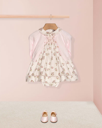 Floral dress on a hanger with pink shoes on the floor against a pink wall