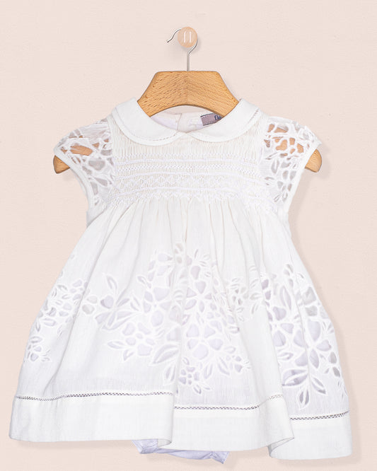 Front view of the Baby Emmy Doppia White Smock Dress Set hanging on a wooden hanger, showcasing floral laser-cut detailing and hand smocking