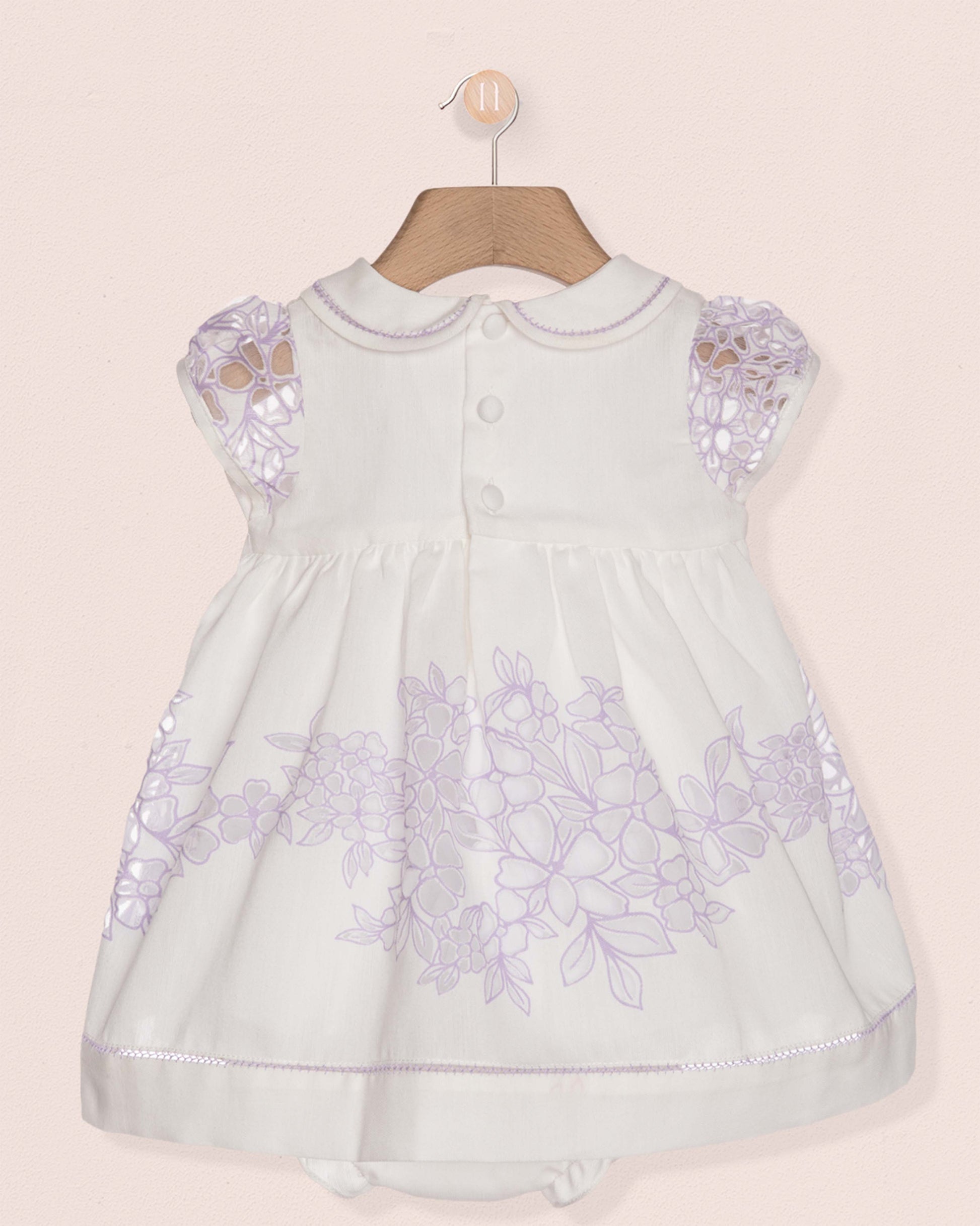 White baby dress with purple floral embroidery on a beige background