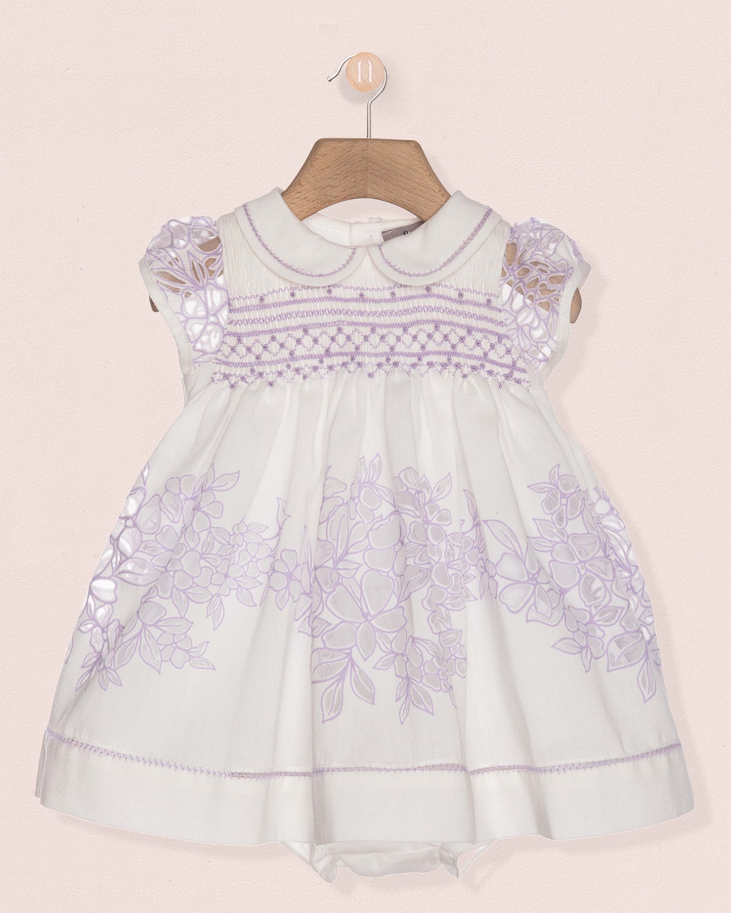 White baby dress with purple floral embroidery on a beige background